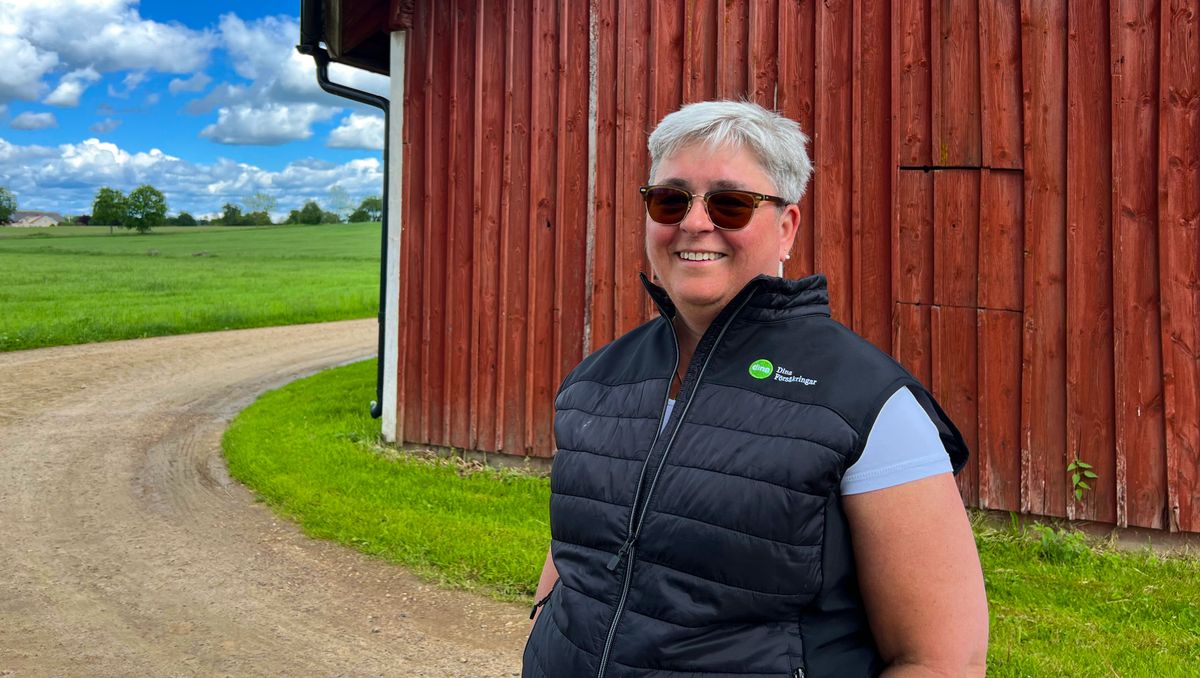 Leende person med solglasögon vid röd lada på landet en solig dag