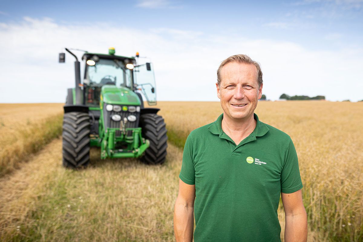 Leende man i grön piké står på sädesfält framför grön traktor